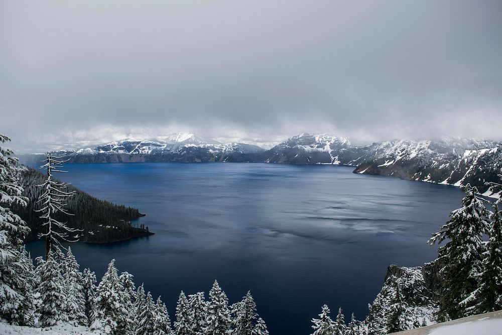Crater Lake with a frozen shoreline of trees under thick gray fog and clouds. Original public domain image from Wikimedia…