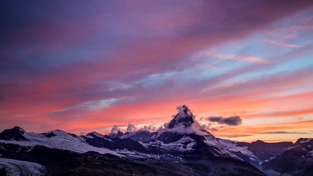 The sun setting over the snow capped Matterhorn mountain, with a blue and orange skyline. Original public domain image from…