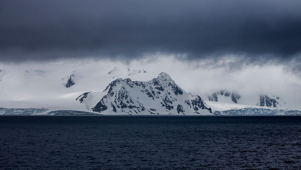Dark clouds amassing over white ridges at the shore in Antarctica. Original public domain image from Wikimedia Commons