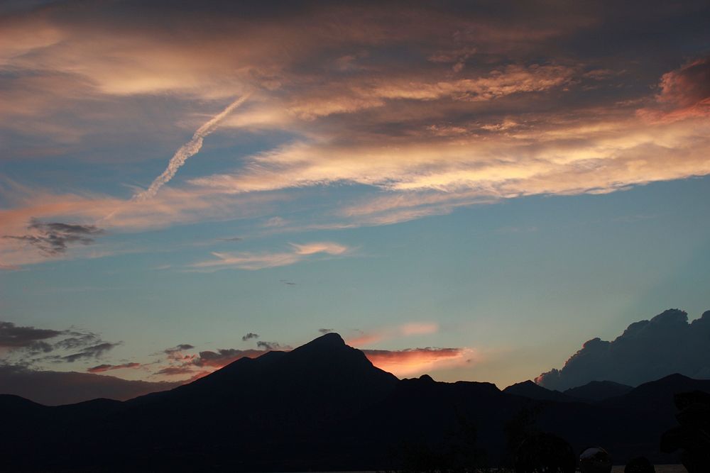 Mountains silhouetted against an evening sky with scattered clouds. Original public domain image from Wikimedia Commons
