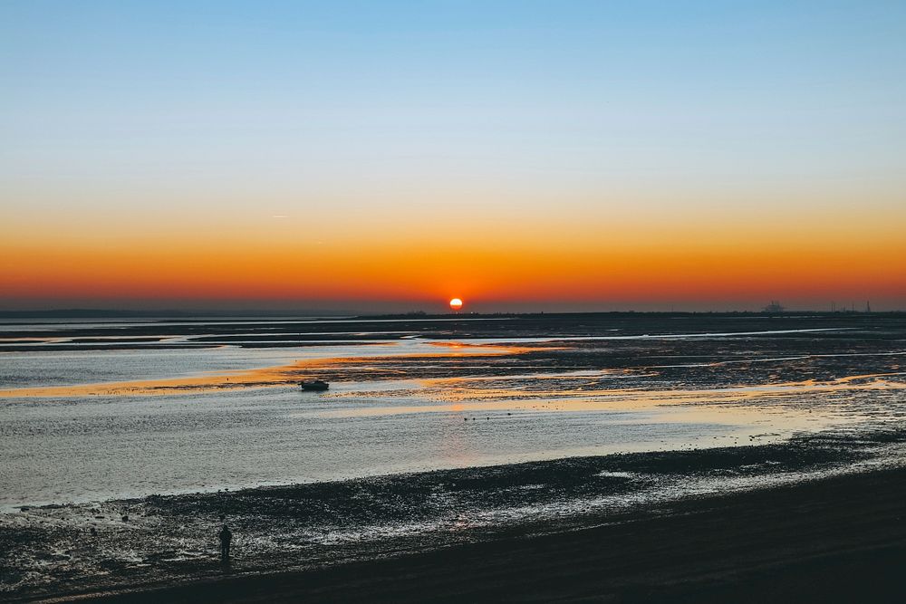 A sun setting on the horizon of a beach in Leigh-on-Sea, Essex as rough ocean waves crash on the coast. Original public…