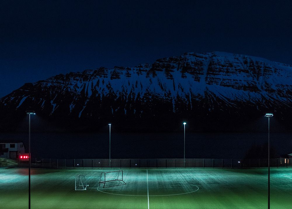 Turf soccer pitch illuminated by floodlights under the snow covered hill at night. Original public domain image from…