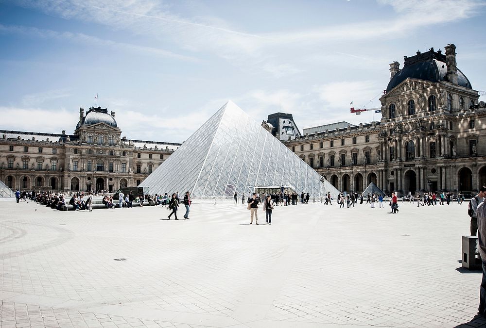 Groups of people walking in front of the glass pyramid in the Louvre courtyard in Paris. Original public domain image from…