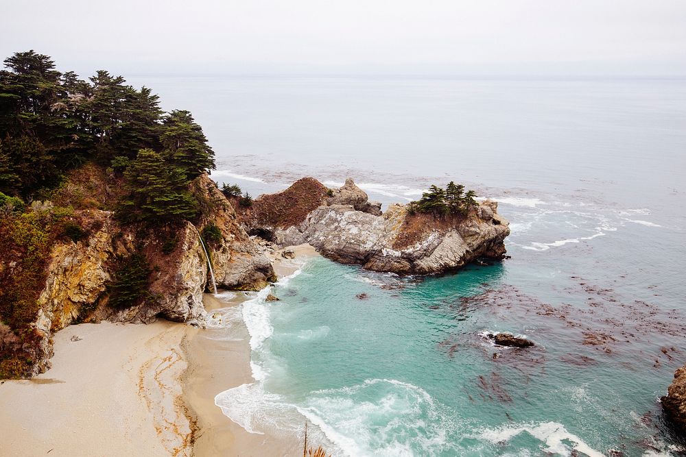 View of rock cliffs and a sand beach by the ocean at McWay Falls. Original public domain image from Wikimedia Commons