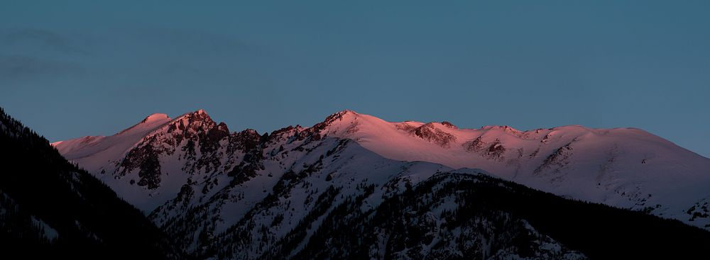 Red light falls on the crest of a snow-topped mountain during sunset. Original public domain image from Wikimedia Commons