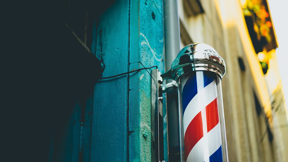 Barbershop red and white swirling pole capped by steel ends beside an aquamarine wall. Original public domain image from…