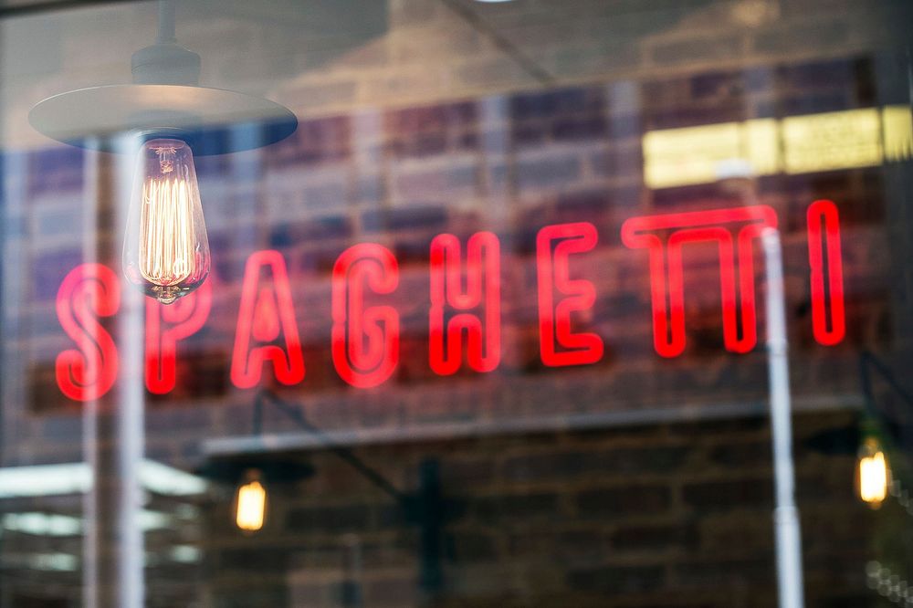 A red neon sign reads "SPAGHETTI" on a wall of a restaurant seen through the window. Original public domain image from…