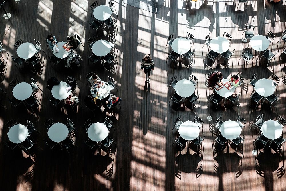Drone view of people eating at white circular tables with the window casting shadows. Original public domain image from…