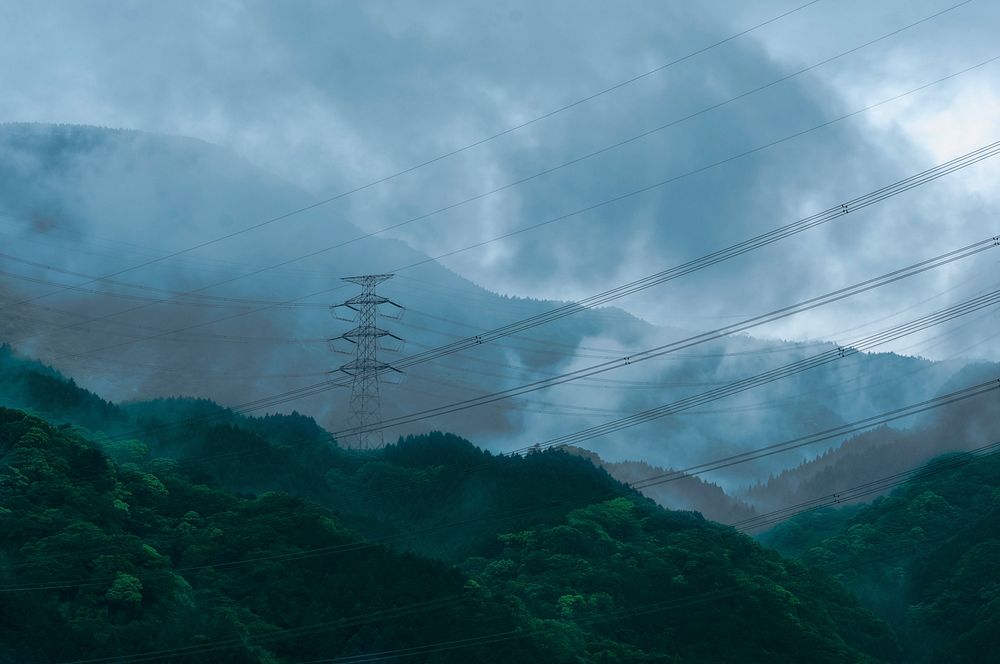 A number of power lines between transmission towers on wooded hills. Original public domain image from Wikimedia Commons