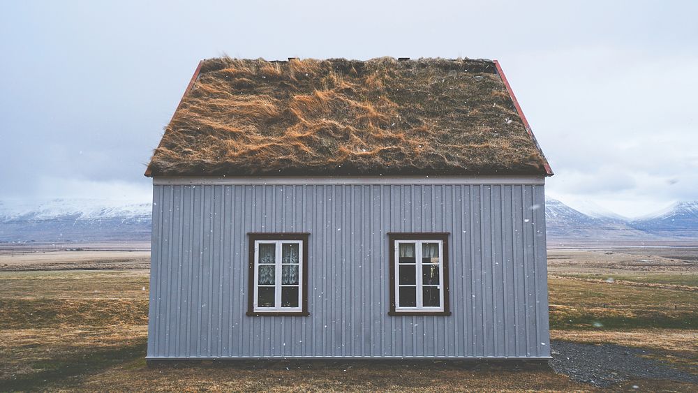 Snowflakes fall in front of a unique house with two windows and a grass roof in Iceland. Original public domain image from…