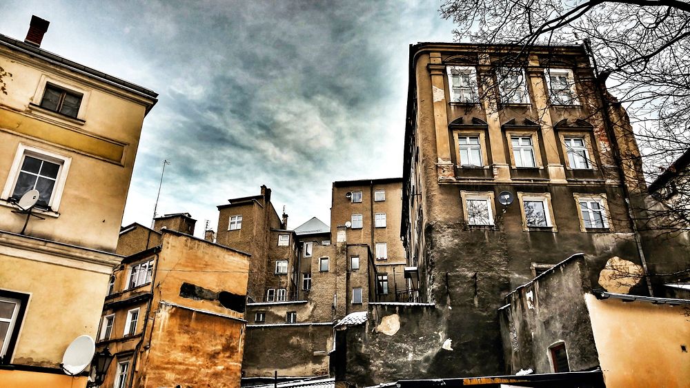 A group of old apartment buildings with fire damage and gray clouds in the background.. Original public domain image from…