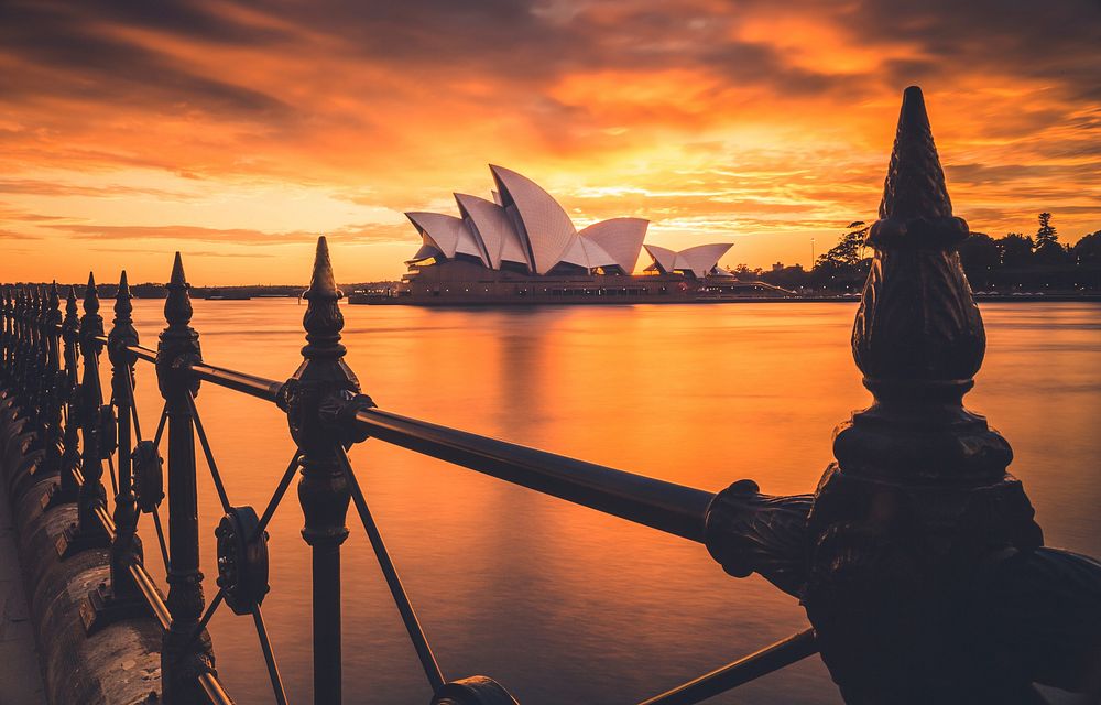 Railing in Sidney with an orange sky during sunset and an opera in the background. Original public domain image from…