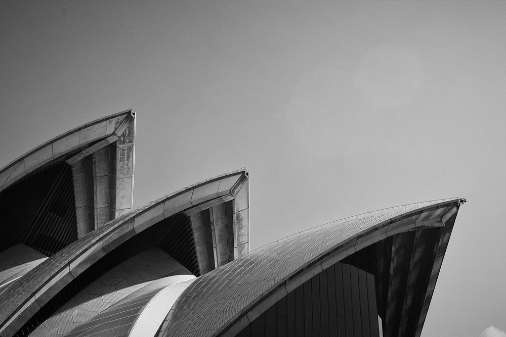 Black and white shot of Sydney Opera House roof architecture with clear sky. Original public domain image from Wikimedia…