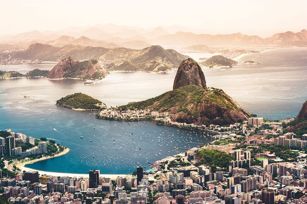 Aerial view of Brazil's Rio de Janeiro and its beaches, buildings, and boats on blue waters, with hills and mountains…