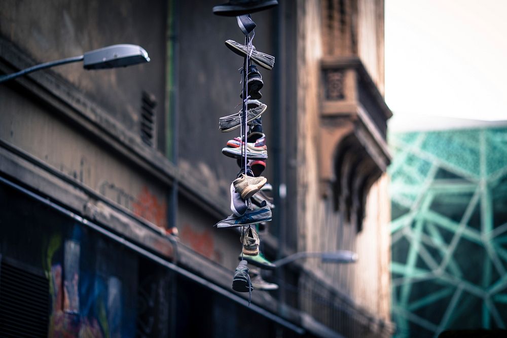 Multiple sneakers lace-tied together hanging from streetlight as tribute in decaying urban area, Hosier Lane. Original…