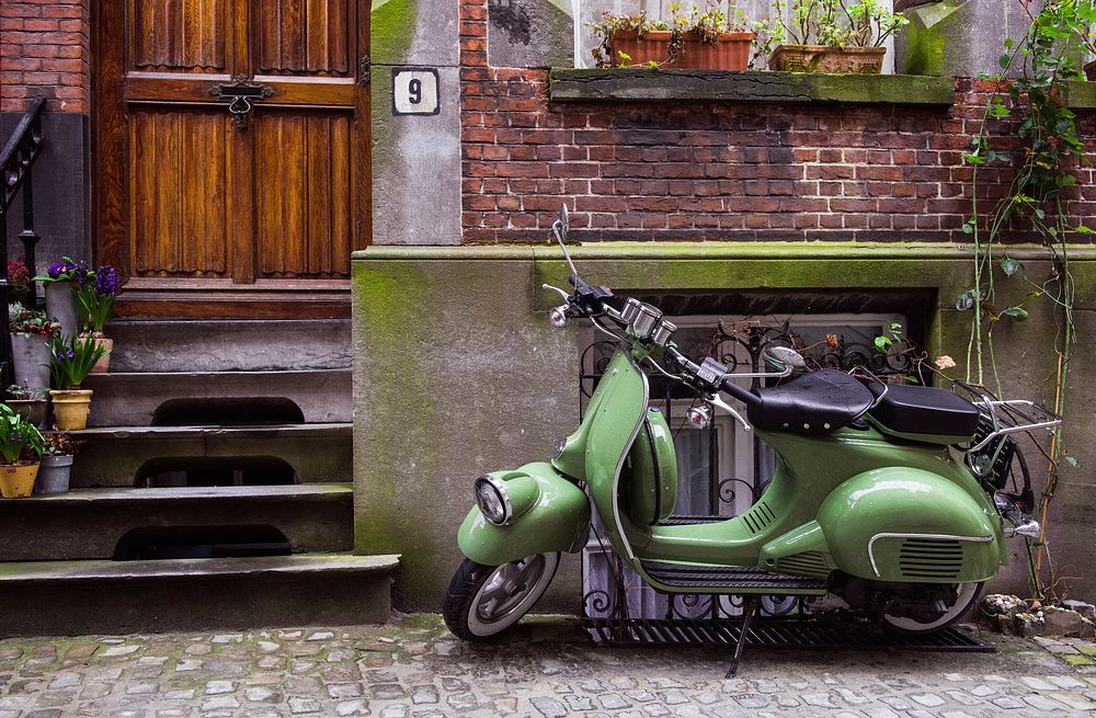 Green scooter sits outside a brick building. Original public domain image from Wikimedia Commons