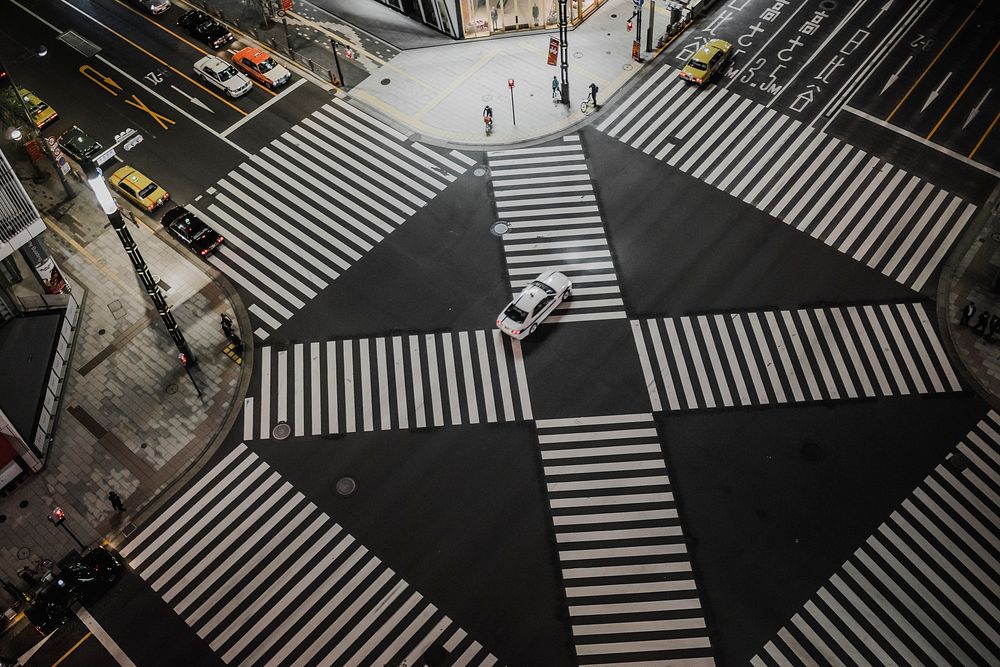 Drone view of crosswalk stripes in intersection in urban area with white car in the center. Original public domain image…