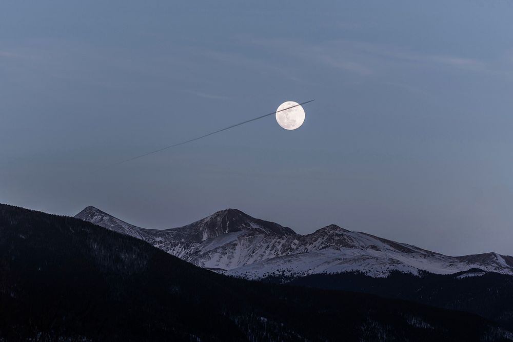 A full moon over mountains during early evening.Original public domain image from Wikimedia Commons