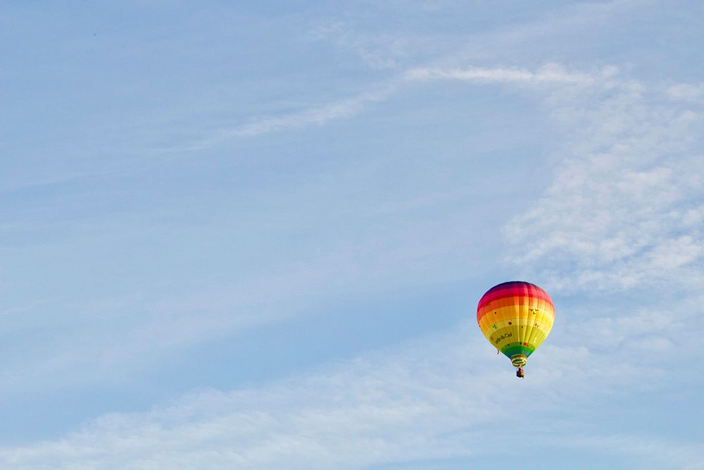 A rainbow-colored hot air balloon against a pale blue sky in Belgium. Original public domain image from Wikimedia Commons