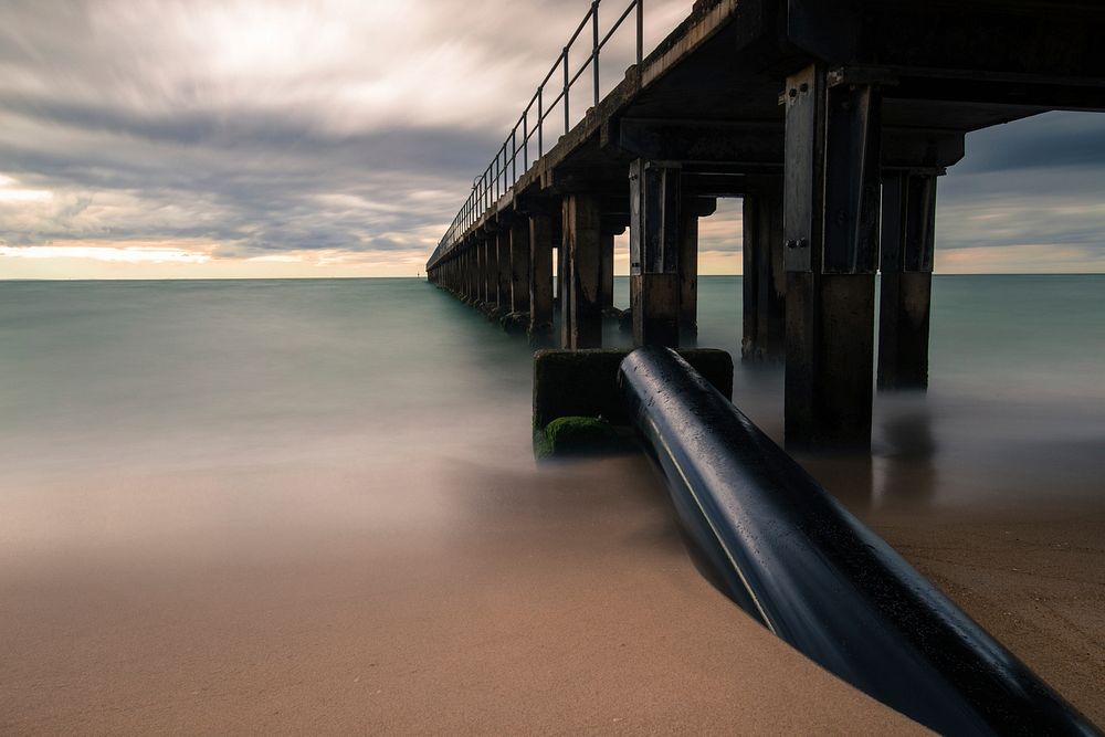 A wooden pier by the ocean in Dromana beach during a cloudy sunset. Original public domain image from Wikimedia Commons