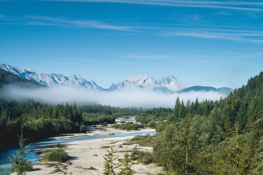 Sandy river banks surrounded by a misty forest with granite mountains on the horizon. Original public domain image from…