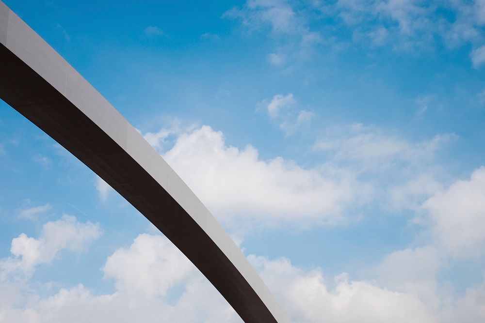 A section of a long concrete arch against a blue sky with fluffy clouds. Original public domain image from Wikimedia Commons