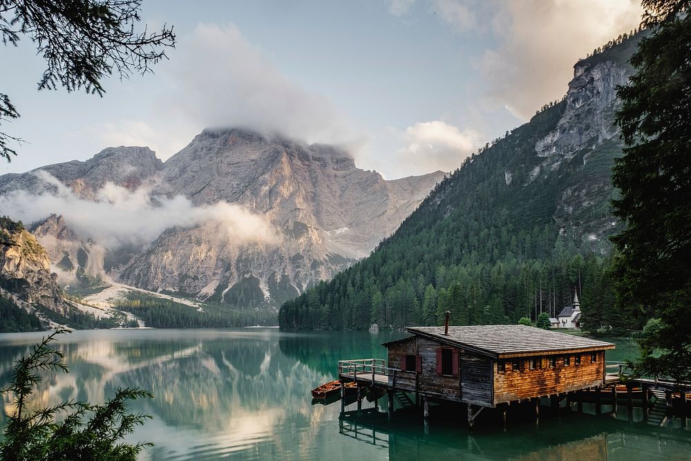 A log cabin lakehouse and dock on Lago di Braies with the snow-capped mountains in the background. Original public domain…