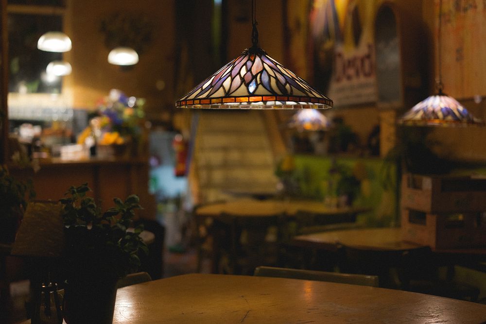 Indoor hanging lamp lights and wooden table in cozy bistro restaurant interior in Amsterdam. Original public domain image…