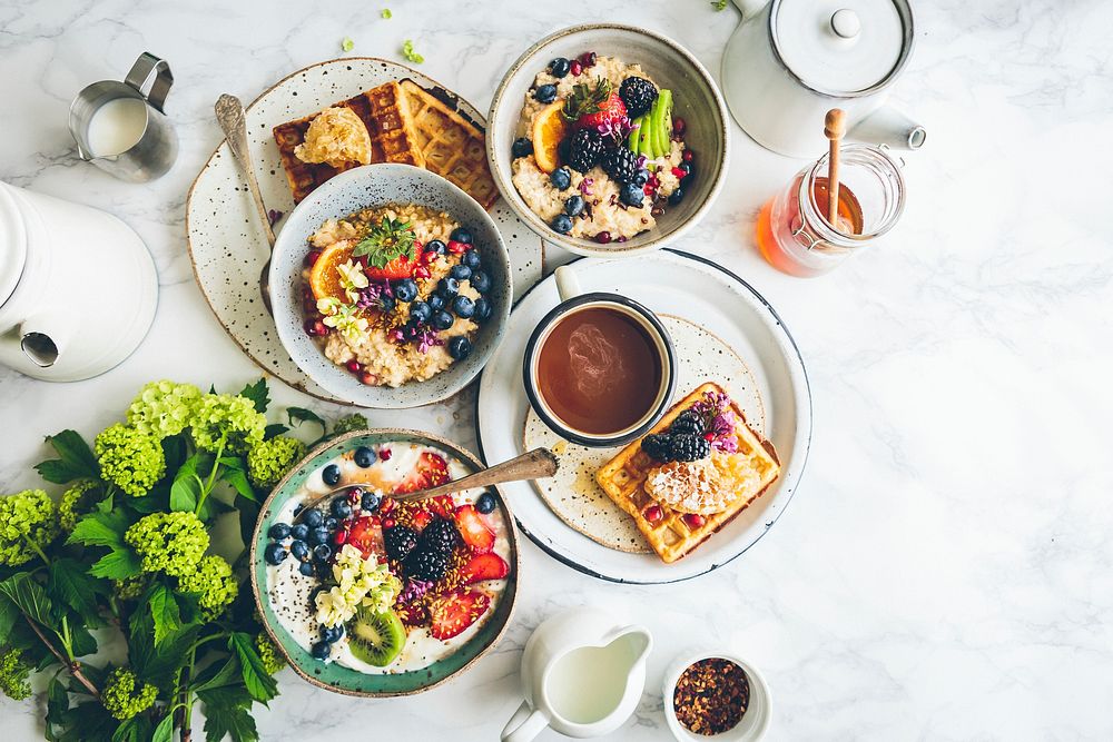 An overhead shot of a waffle, bowls of fruit oatmeal and a cup of coffee. Original public domain image from Wikimedia Commons