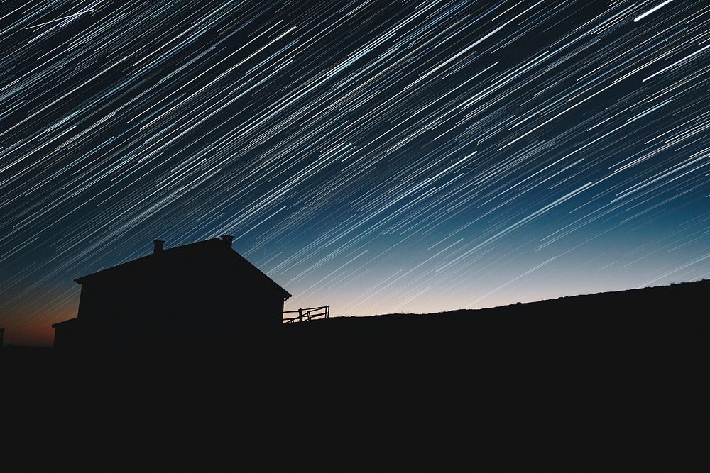 Long exposure photograph of the star trails above the silhouette of a house. Original public domain image from Wikimedia…
