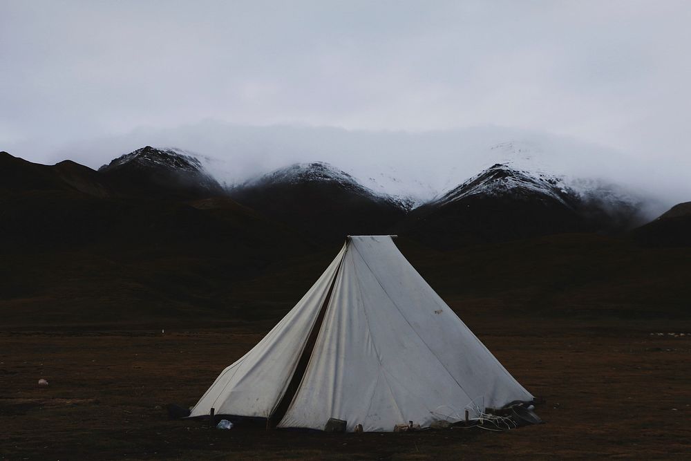 White tent set up in the grass with snowy mountains in the background. Original public domain image from Wikimedia Commons