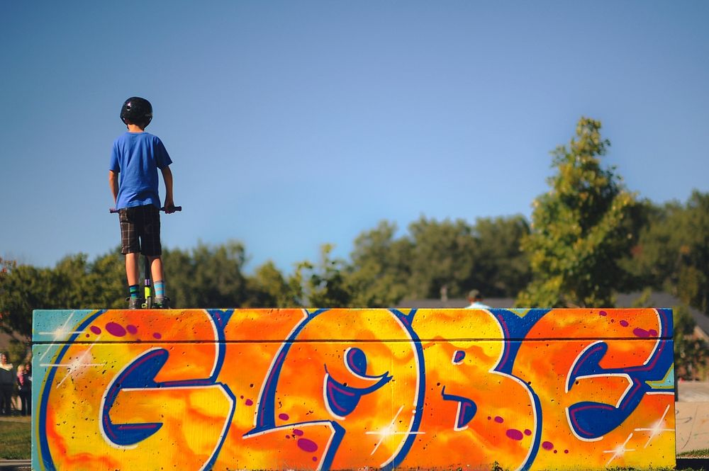 Young child stands atop a graffiti ramp at a skate park. Original public domain image from Wikimedia Commons