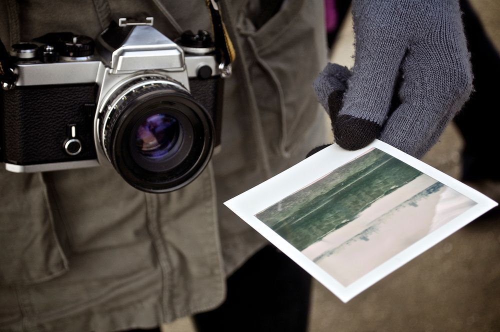 A close-up of a camera and a man wearing gloves holding a photograph.. Original public domain image from Wikimedia Commons