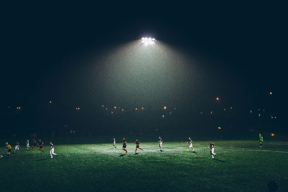 A soccer game being played at night under floodlights. Original public domain image from Wikimedia Commons