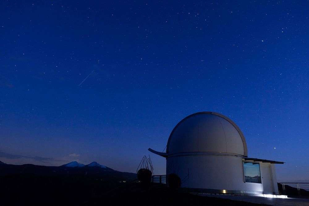 Observatory telescope watching the blue, night sky with mountains in the background. Original public domain image from…