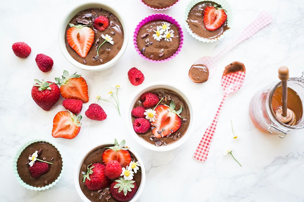 Cupcake filters and bowls filled with chocolate mixture, chocolate pieces, strawberries, raspberries, and daisies beside…