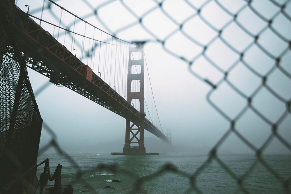 Aerial view from a chain link fence of the San Francisco golden gate bridge covered by fog. Original public domain image…