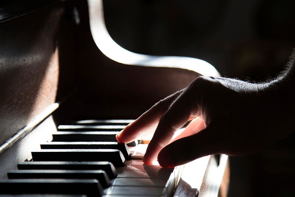A person's hand playing the piano in the light. Original public domain image from Wikimedia Commons