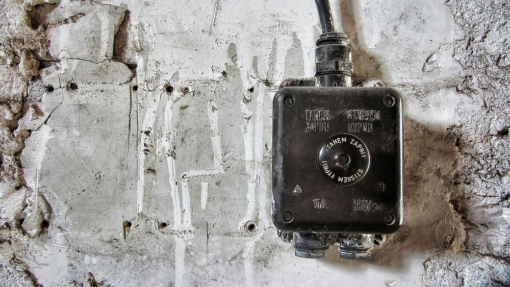 Old black electric box situated on a gray concrete wall. Original public domain image from Wikimedia Commons