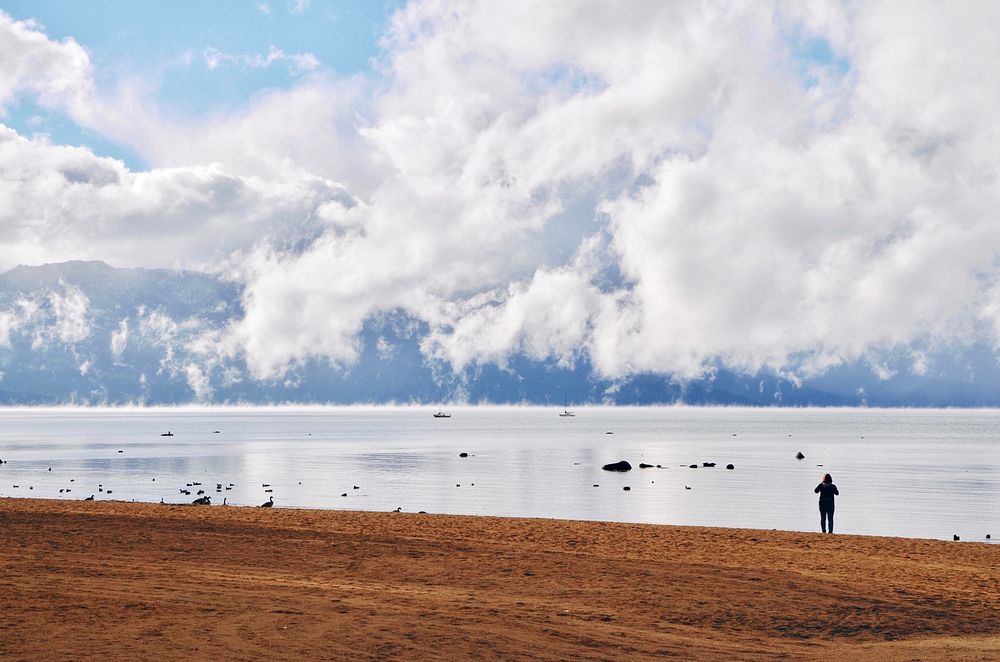Person on the sandy beach looking at the clouds above Lake Tahoe. Original public domain image from Wikimedia Commons