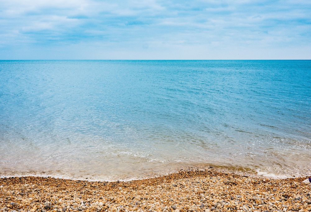 Sandy beach, blue ocean, stones, clear sky. Original public domain image from Wikimedia Commons