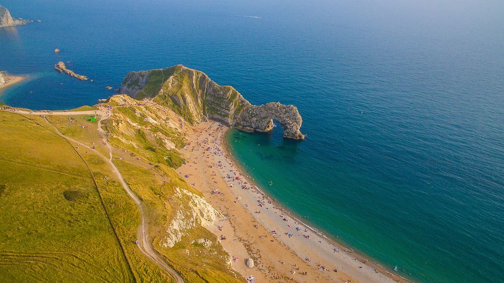 Drone aerial view of a cliff with green fields on the ocean sand shoreline at Durdle Door. Original public domain image from…