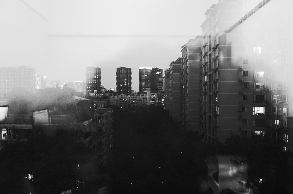 A fuzzy black-and-white shot of an apartment complex seen through a window. Original public domain image from Wikimedia…