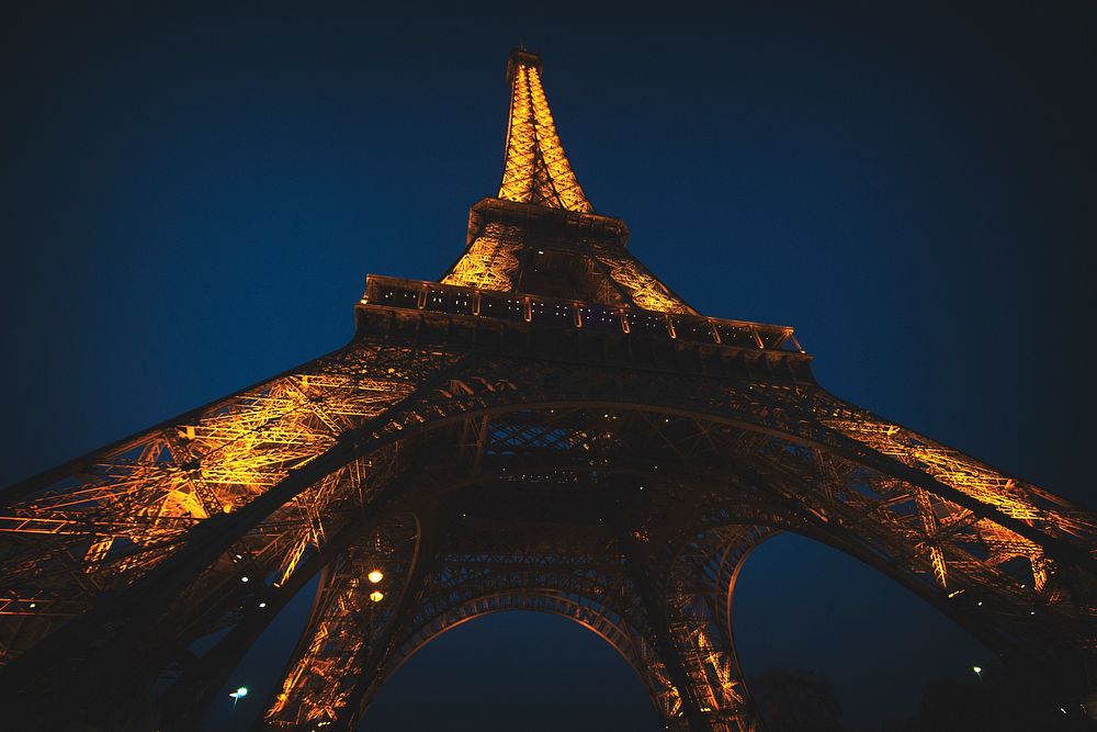 Looking up at the Eiffel Tower illuminated at night in Paris. Original public domain image from Wikimedia Commons
