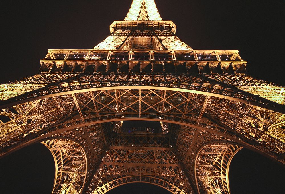 A centered shot looking up at the Eiffel Tower in Paris illuminated at night. Original public domain image from Wikimedia…