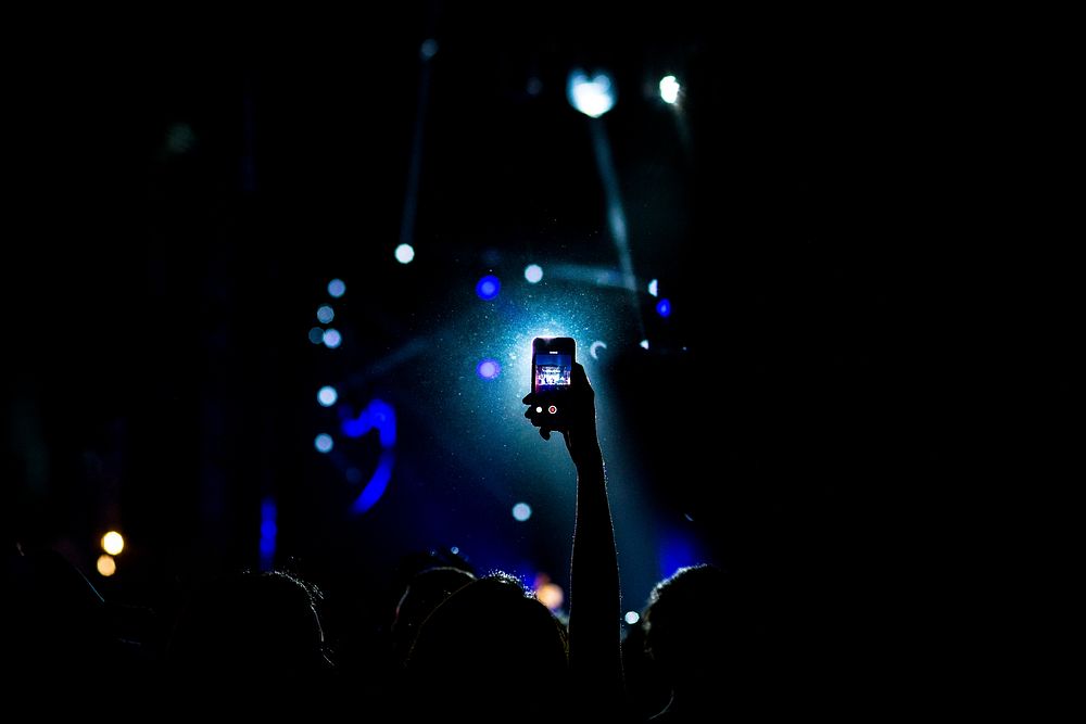 The silhouette of a person holding up their iPhone cellphone at a concert in Monterrey. Original public domain image from…