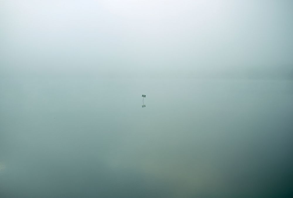 Single isolated sign sits in eerie still waters covered in clouds. Original public domain image from Wikimedia Commons