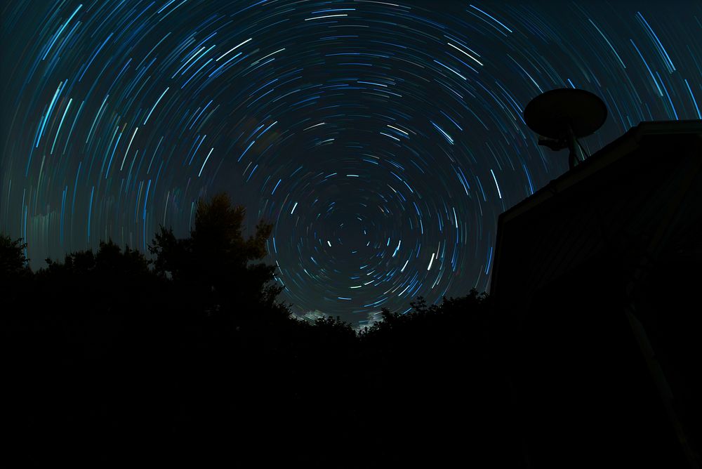 Star trail above the silhouette of trees and rooftop. Original public domain image from Wikimedia Commons