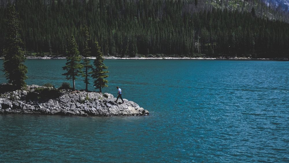 A man walking on a rocky shore of a lake. Original public domain image from Wikimedia Commons