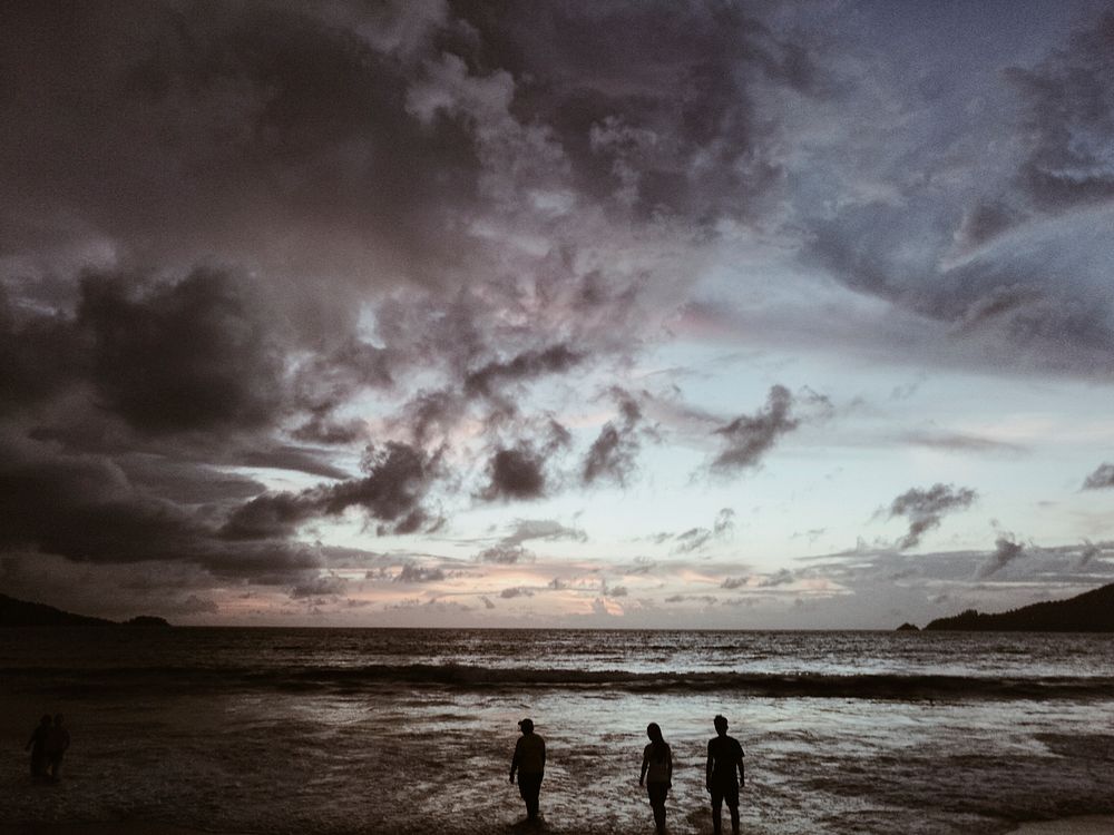 Three silhouettes looking at the stormy skies by the ocean in Patong, Phuket, Thailand. Original public domain image from…